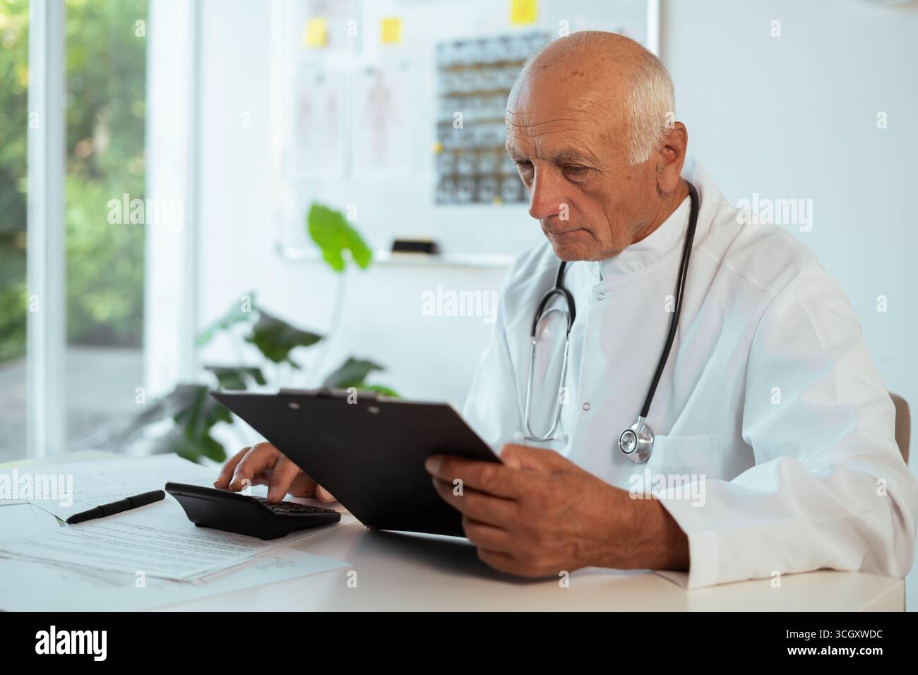 Docteur comptable masculin senior âgé en manteau blanc avec stéthoscope calculant les finances de comptabilité et le budget de l'hôpital à l'intérieur de la clinique, concept o Banque D'Images