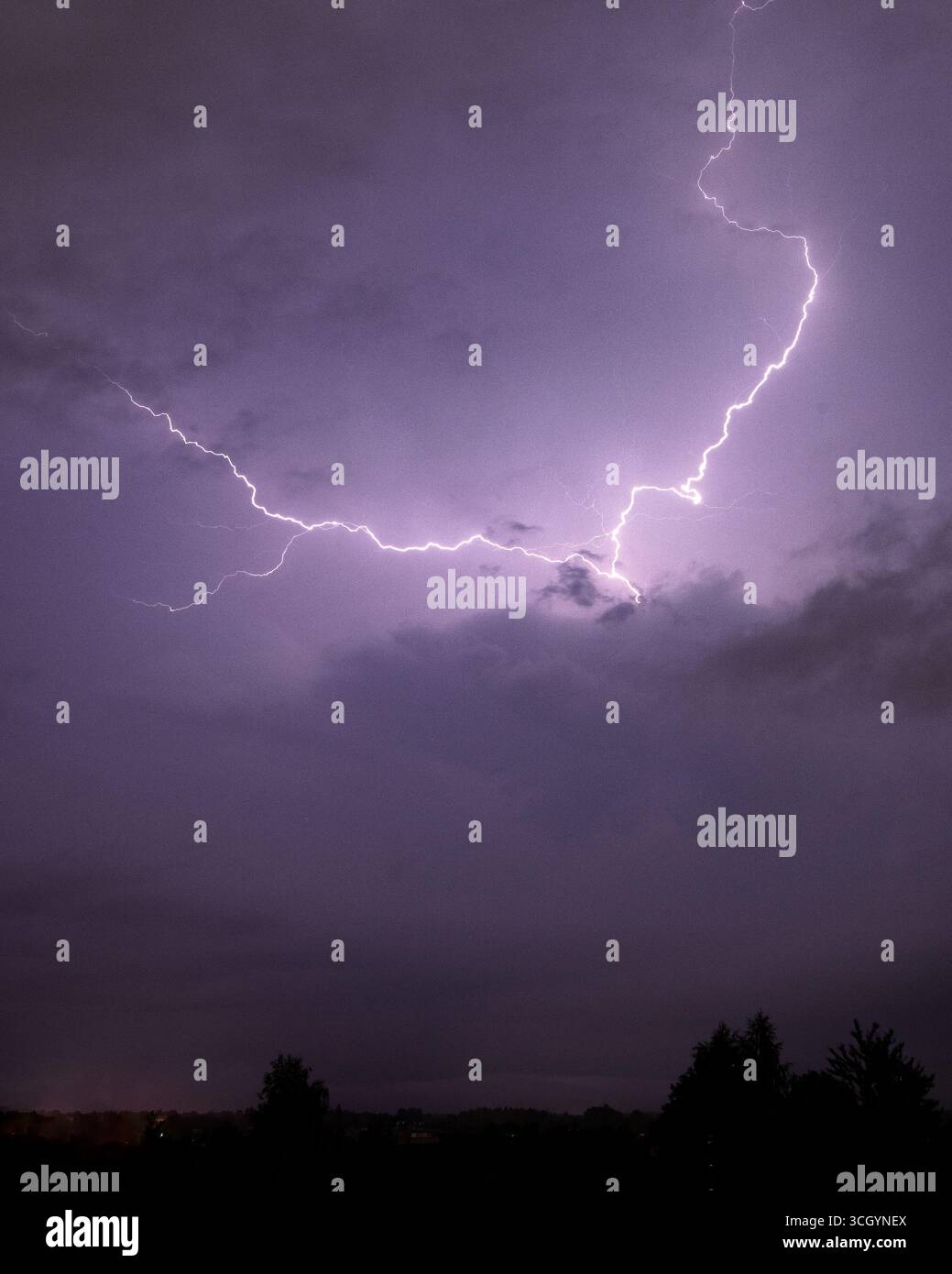 Un éclair déchiqueté déchire un ciel orageux violet dramatique, illuminant la nuit d'une intensité électrique. Banque D'Images