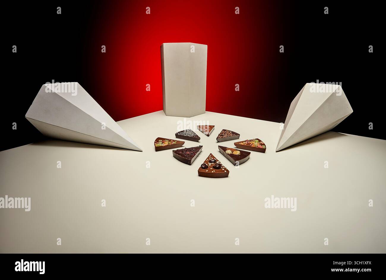 Disposition symétrique comportant des tranches de barres de chocolat disposées en forme circulaire sur une surface blanche, accentuées par des formes de prismes angulaires et des bef Banque D'Images