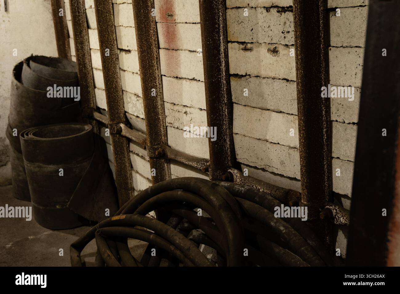 Tunnel de service minier abandonné avec nervures en acier, revêtement en blocs de béton et tuyaux enroulés sur le sol, illustrant le vieillissement de l'infrastructure de sécurité. Banque D'Images