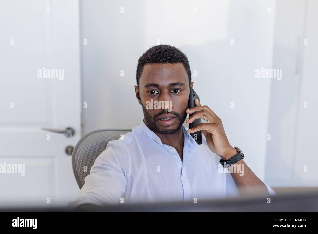 Homme d'affaires parlant sur smartphone tout en travaillant sur l'ordinateur au bureau Banque D'Images