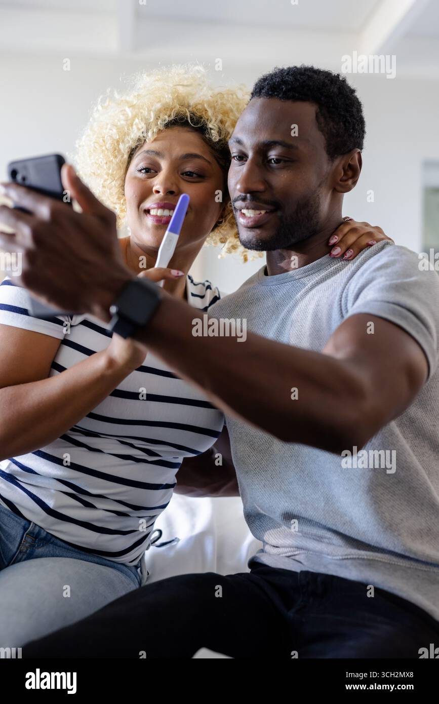 Couple célébrant un résultat positif de test de grossesse tout en prenant selfie à la maison Banque D'Images