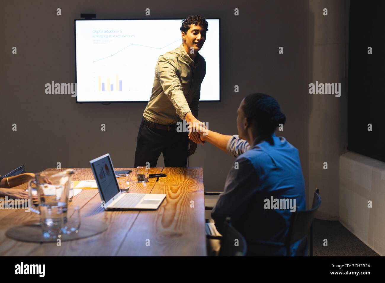Professionnels se serrant la main lors de la réunion du soir avec écran de présentation Banque D'Images Professionnels se serrant la main lors de la réunion du soir avec écran de présentation Banque D'Images