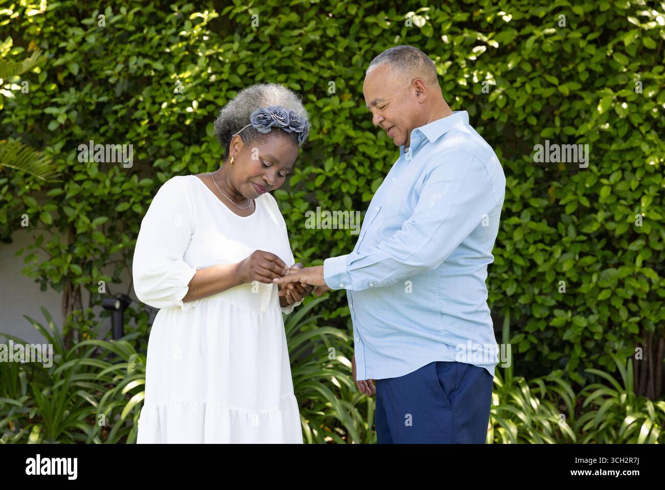 Couple senior échangeant des anneaux dans le jardin, partageant un moment joyeux ensemble Banque D'Images