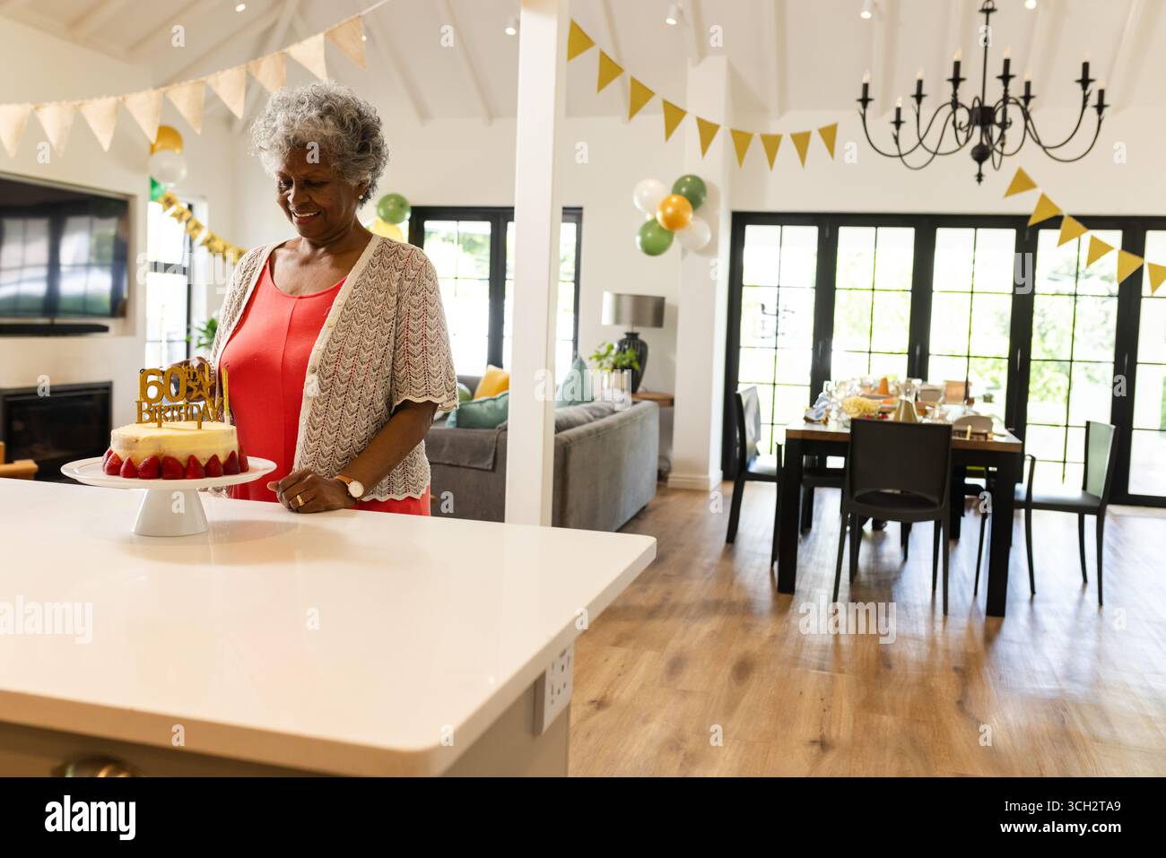 Femme senior tenant le gâteau de 60e anniversaire derrière l'îlot de cuisine dans le salon ouvert, espace de copie Banque D'Images