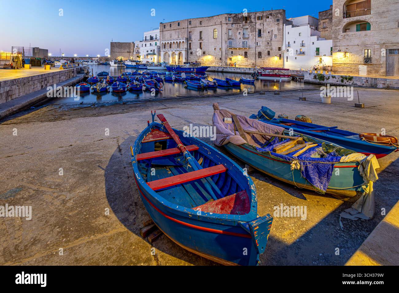 Bateaux de pêche en bois colorés amarrés dans le vieux port de Monopoli, Pouilles, Italie, avec des bâtiments historiques en pierre illuminés au crépuscule. Photo prise le Banque D'Images