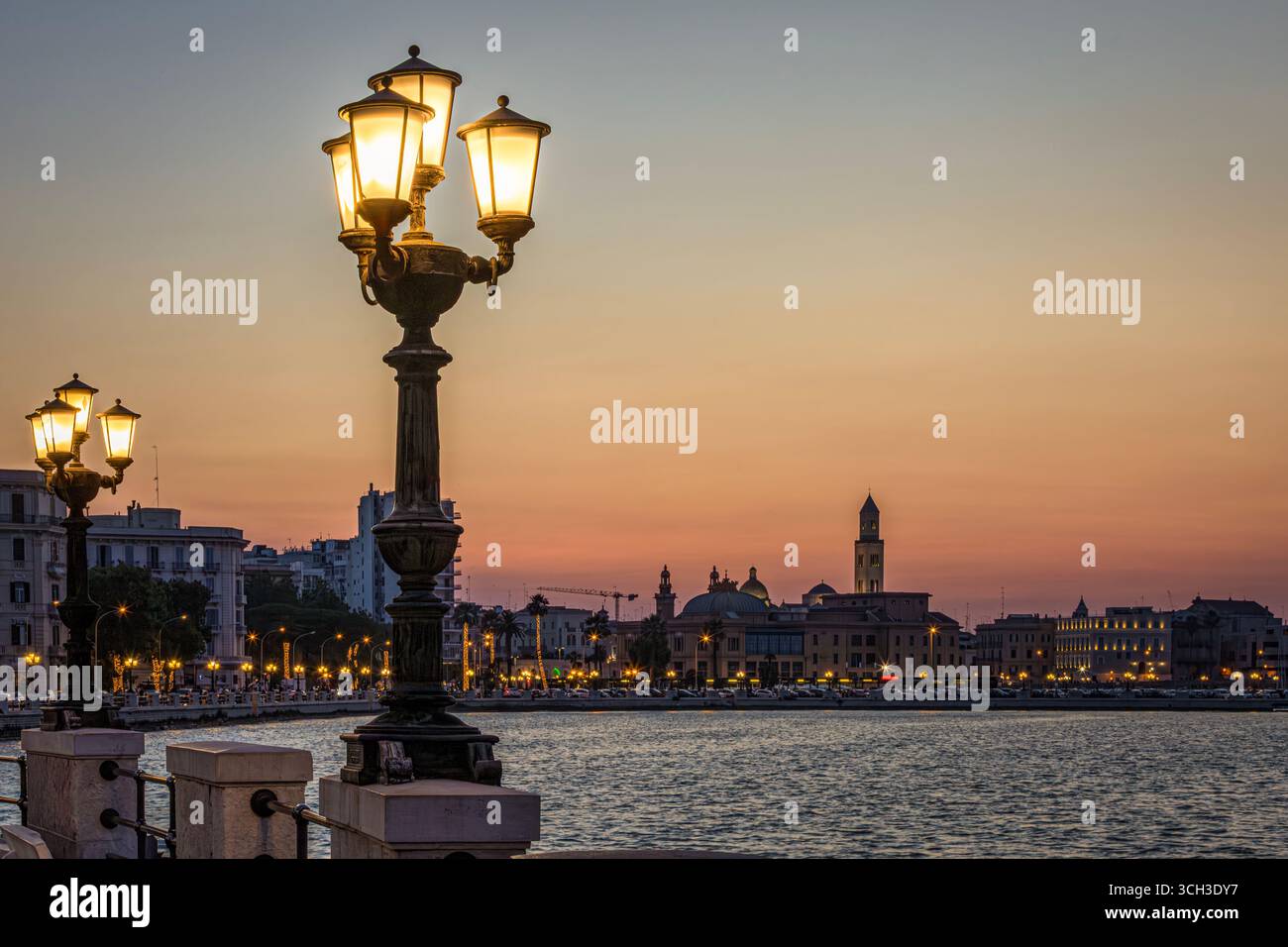 Promenade illuminée et silhouettes emblématiques de Bari, Italie, au crépuscule, avec un ciel orange vibrant. Photo prise le 21 juin 2025. Banque D'Images