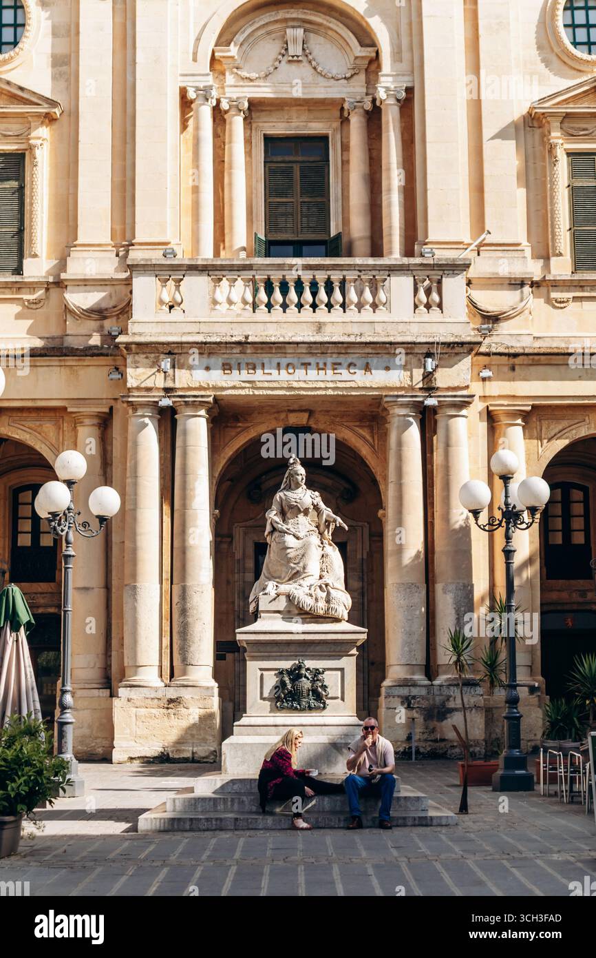 La Valette, Malte - 10 avril 2025 : la statue de la reine Victoria assise devant la Bibliothèque nationale de Malte, également connue sous le nom de Bibliotheca Banque D'Images