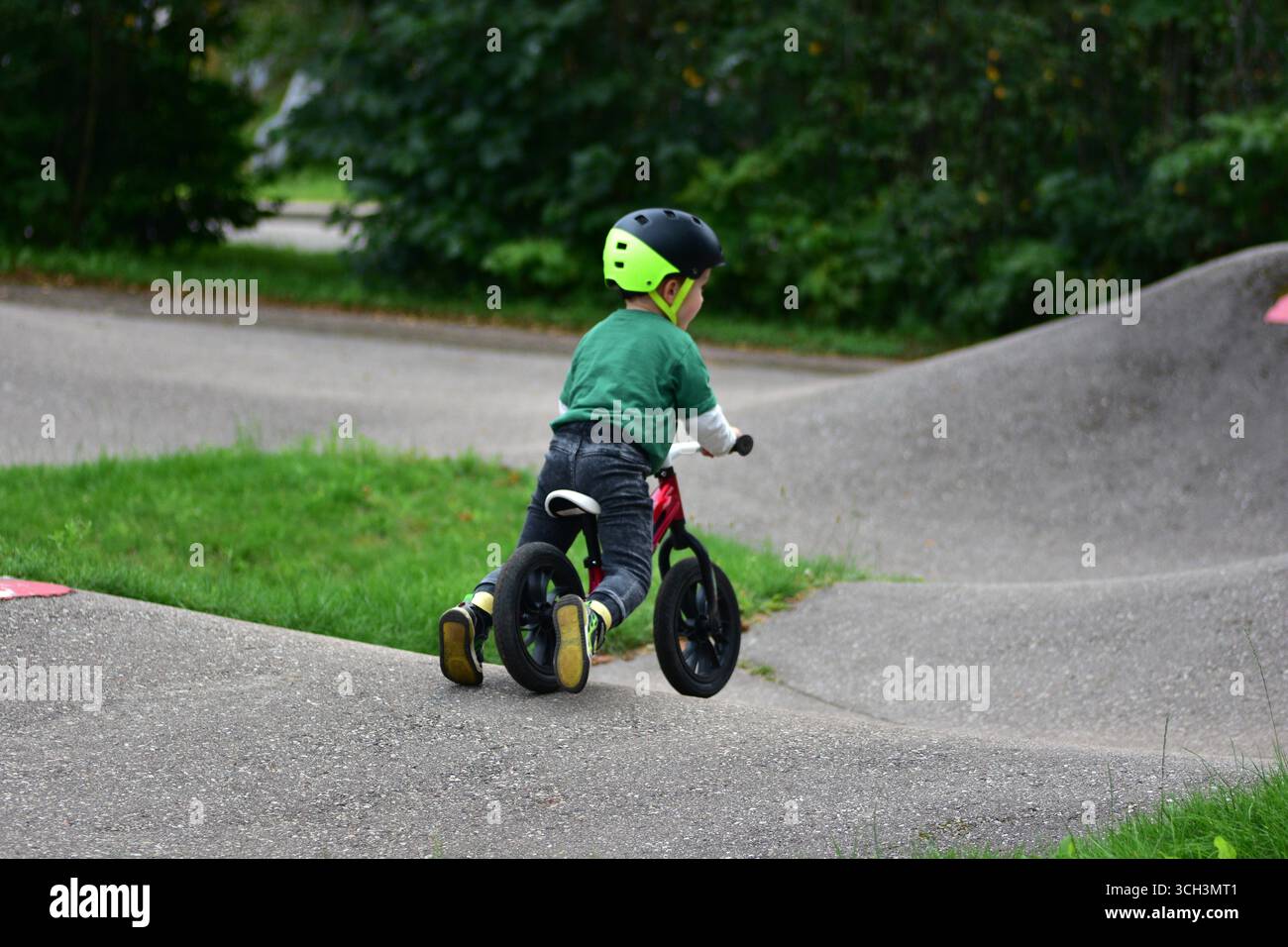 Garçon en bas âge portant un casque roule vélo d'équilibre rouge sur la piste de pompe d'asphalte. Apprentissage actif de l'équilibre et de la coordination de l'enfant tout en jouant en plein air Banque D'Images