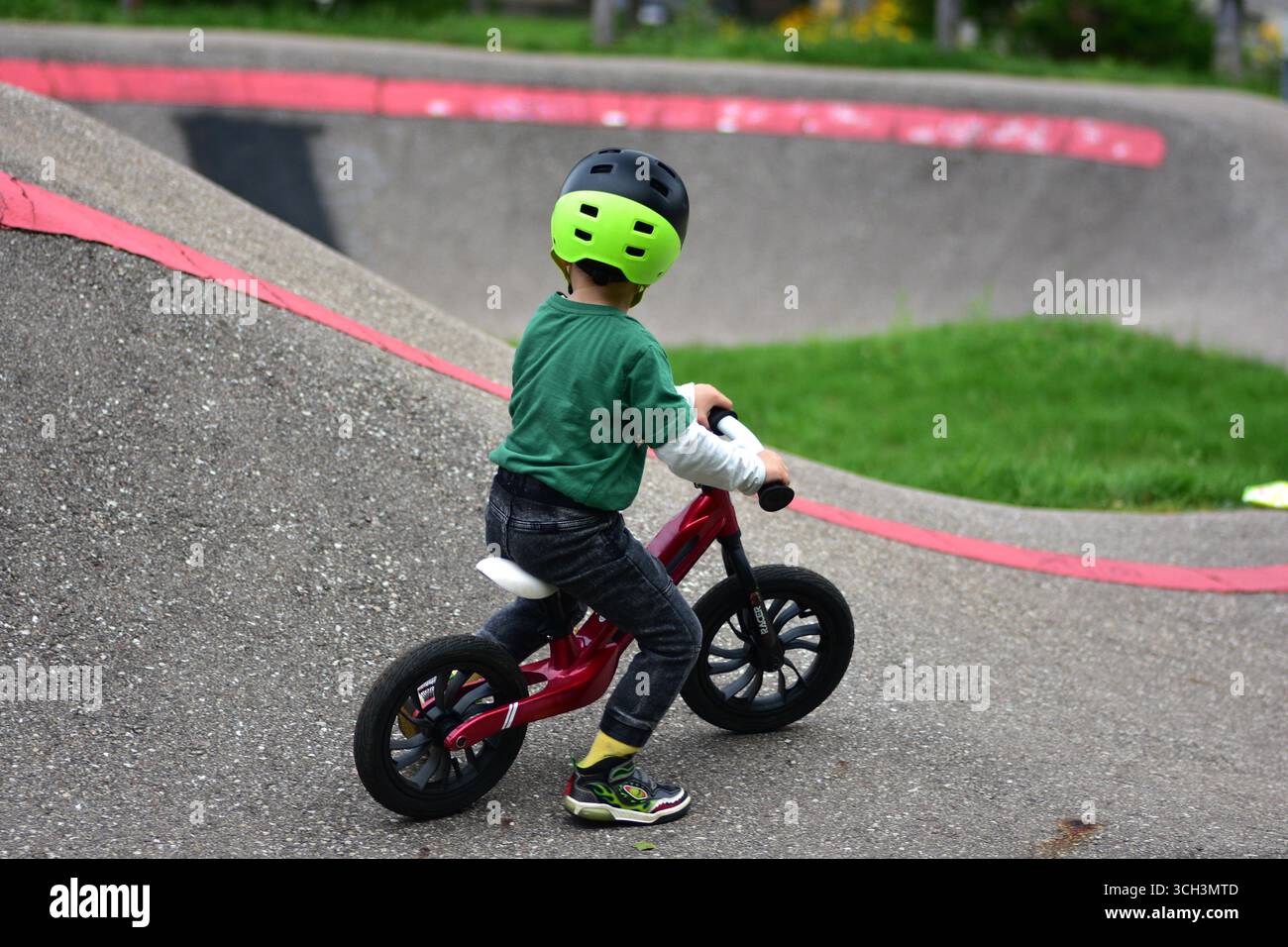 Garçon en bas âge portant un casque roule vélo d'équilibre rouge sur la piste de pompe d'asphalte. Apprentissage actif de l'équilibre et de la coordination de l'enfant tout en jouant en plein air Banque D'Images