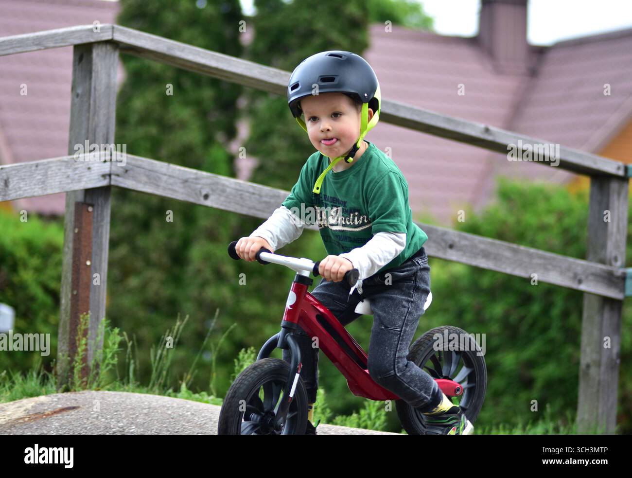 Garçon en bas âge portant un casque roule vélo d'équilibre rouge sur la piste de pompe d'asphalte. Apprentissage actif de l'équilibre et de la coordination de l'enfant tout en jouant en plein air Banque D'Images