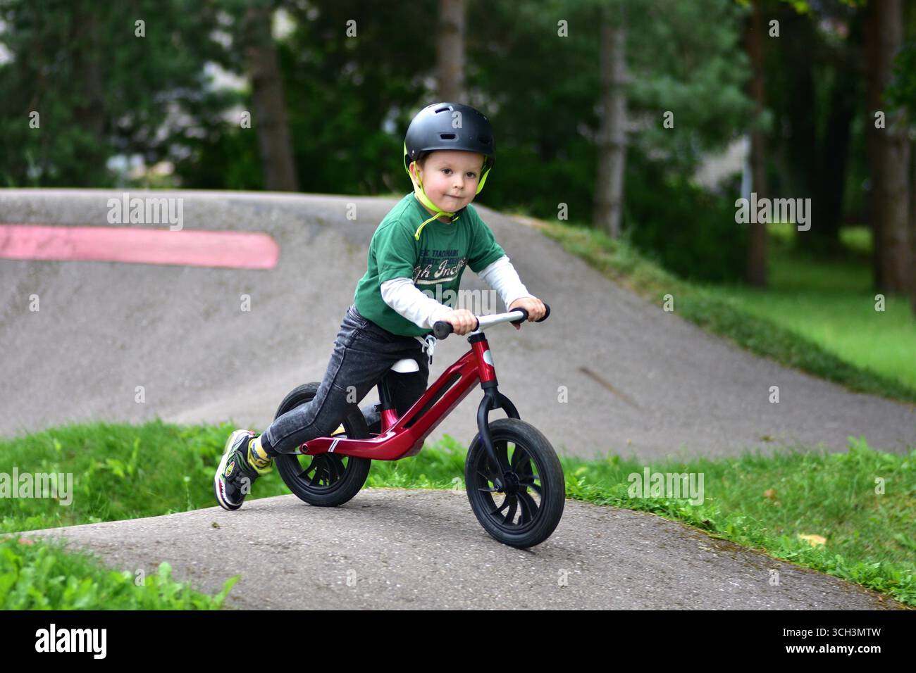 Garçon en bas âge portant un casque roule vélo d'équilibre rouge sur la piste de pompe d'asphalte. Apprentissage actif de l'équilibre et de la coordination de l'enfant tout en jouant en plein air Banque D'Images