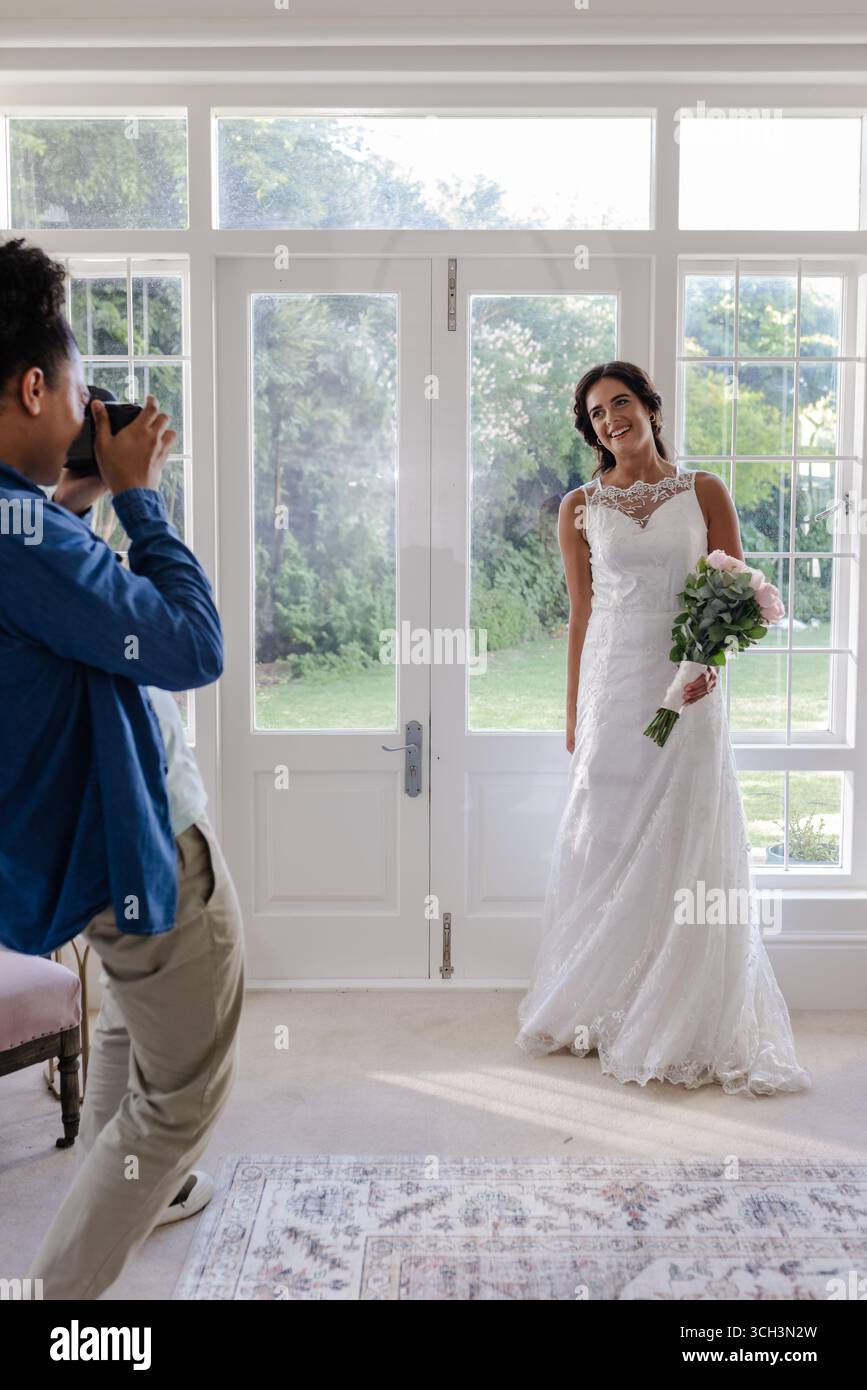 Mariée en élégante robe blanche posant avec bouquet tandis que le photographe capture le moment Banque D'Images