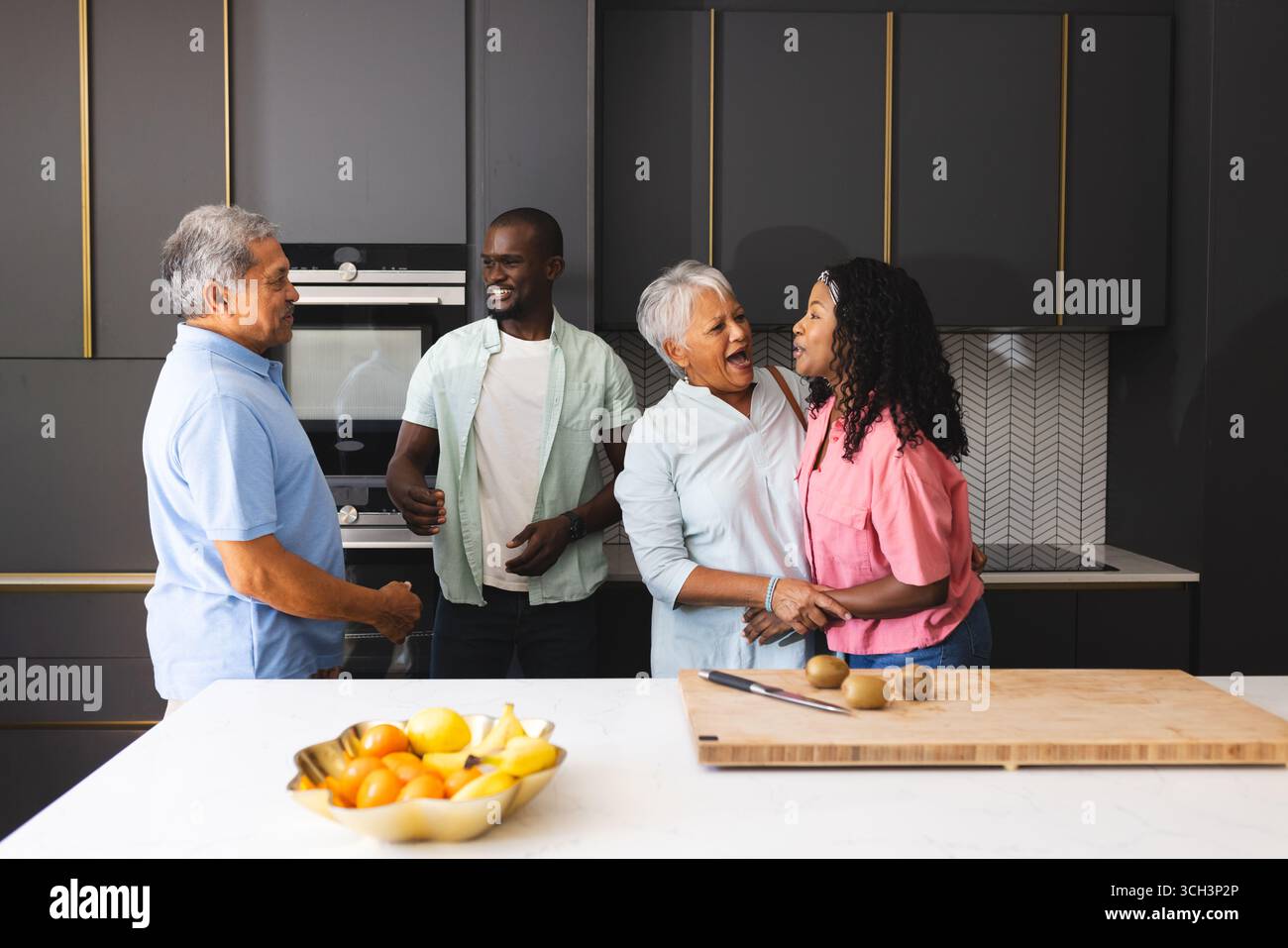 Famille heureuse multigénérationnelle rire et se lier dans une cuisine moderne avec des fruits frais, à la maison Banque D'Images Famille heureuse multigénérationnelle rire et se lier dans une cuisine moderne avec des fruits frais, à la maison Banque D'Images