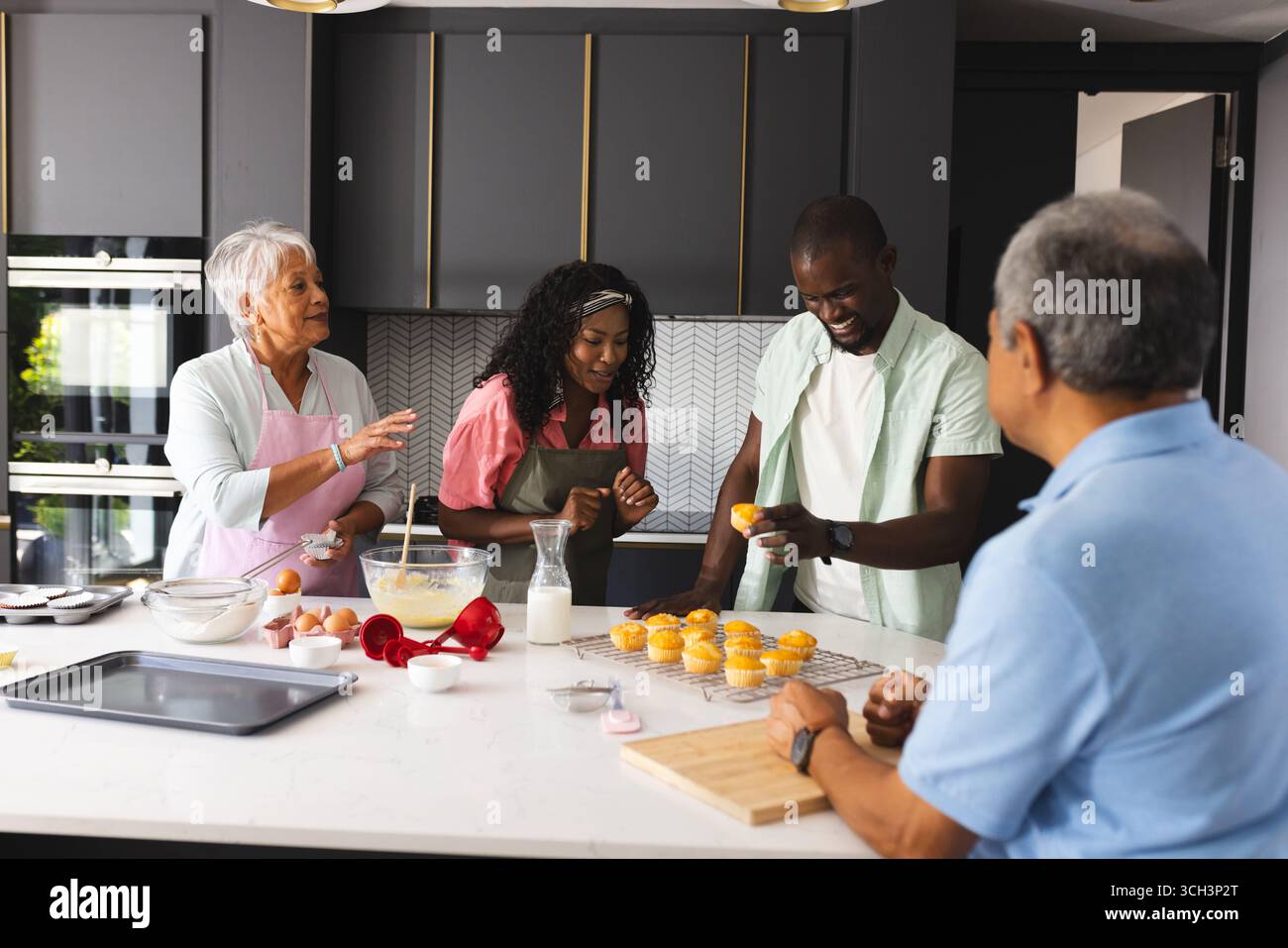 Famille heureuse cuisiner dans une cuisine moderne, partager le rire et décorer des cupcakes, à la maison Banque D'Images Famille heureuse cuisiner dans une cuisine moderne, partager le rire et décorer des cupcakes, à la maison Banque D'Images