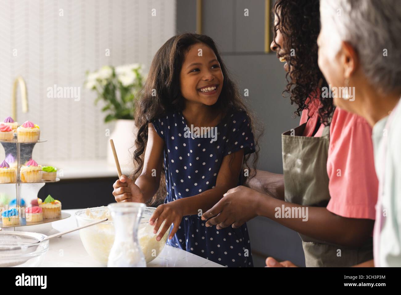 Trois générations heureuses cuisiner en cuisine, partager des sourires et faire des cupcakes, à la maison Banque D'Images Trois générations heureuses cuisiner en cuisine, partager des sourires et faire des cupcakes, à la maison Banque D'Images