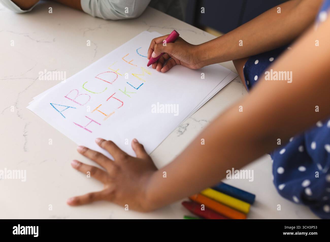 Enfant pratiquant l'écriture alphabétique avec des crayons colorés sur papier à la maison Banque D'Images Enfant pratiquant l'écriture alphabétique avec des crayons colorés sur papier à la maison Banque D'Images
