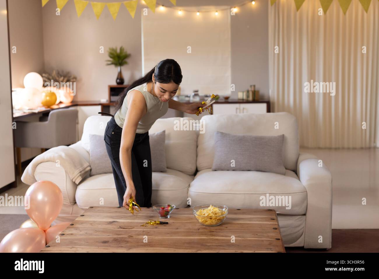 jeune femme plaçant des poppers de fête dorés sur la table basse dans le salon avec des ballons, copiez l'espace Banque D'Images