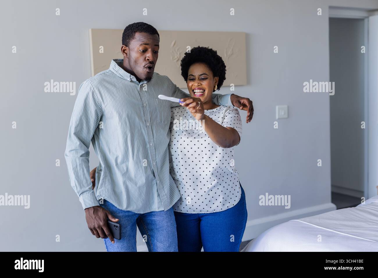 Couple célébrant un résultat positif de test de grossesse à la maison, embrassant avec joie Banque D'Images