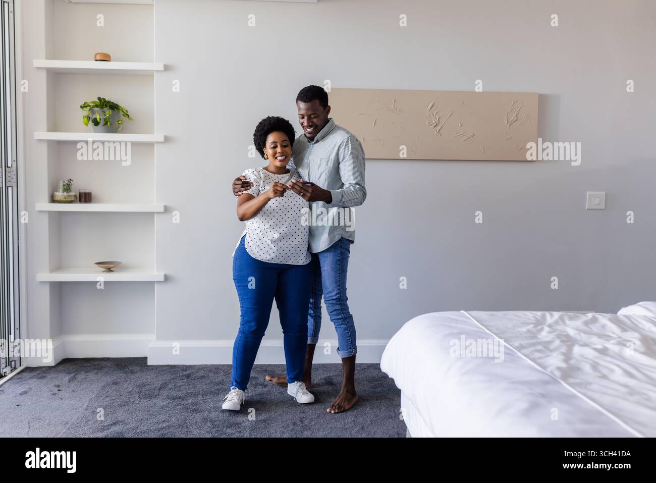 Couple à la maison souriant tout en regardant smartphone ensemble dans la chambre Banque D'Images