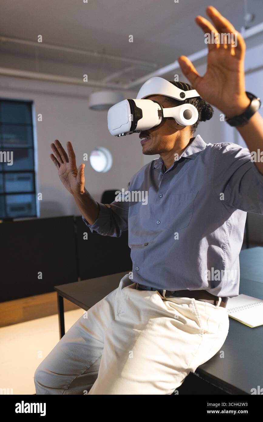 Homme utilisant un casque VR dans le bureau, s'engageant avec l'environnement virtuel avec enthousiasme Banque D'Images Homme utilisant un casque VR dans le bureau, s'engageant avec l'environnement virtuel avec enthousiasme Banque D'Images