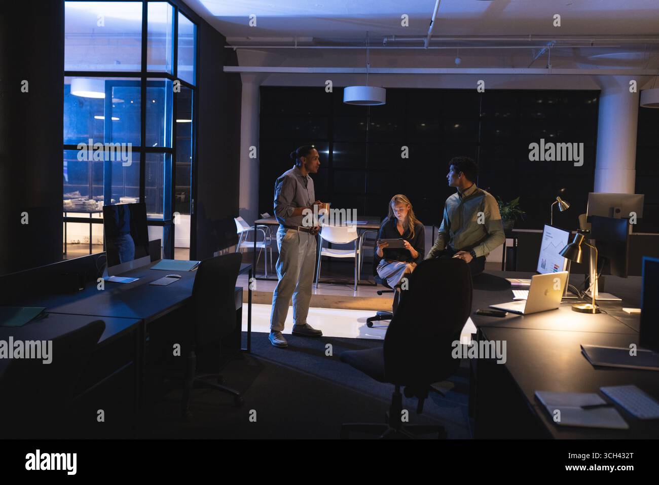 Professionnels collaborant dans un bureau moderne la nuit, discutant des détails du projet Banque D'Images Professionnels collaborant dans un bureau moderne la nuit, discutant des détails du projet Banque D'Images