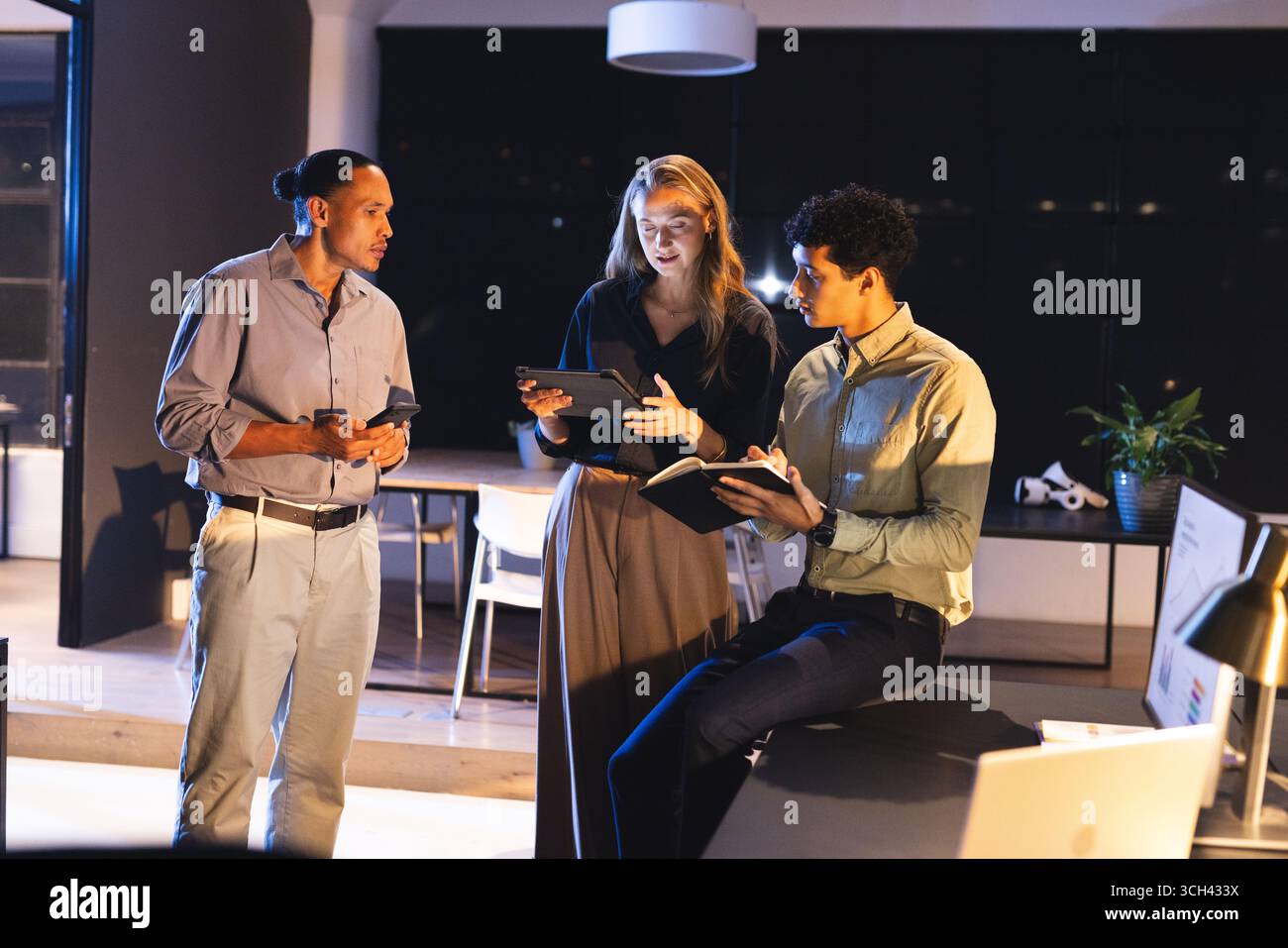 Équipe d'affaires collaborant sur des appareils numériques dans un bureau moderne la nuit Banque D'Images
