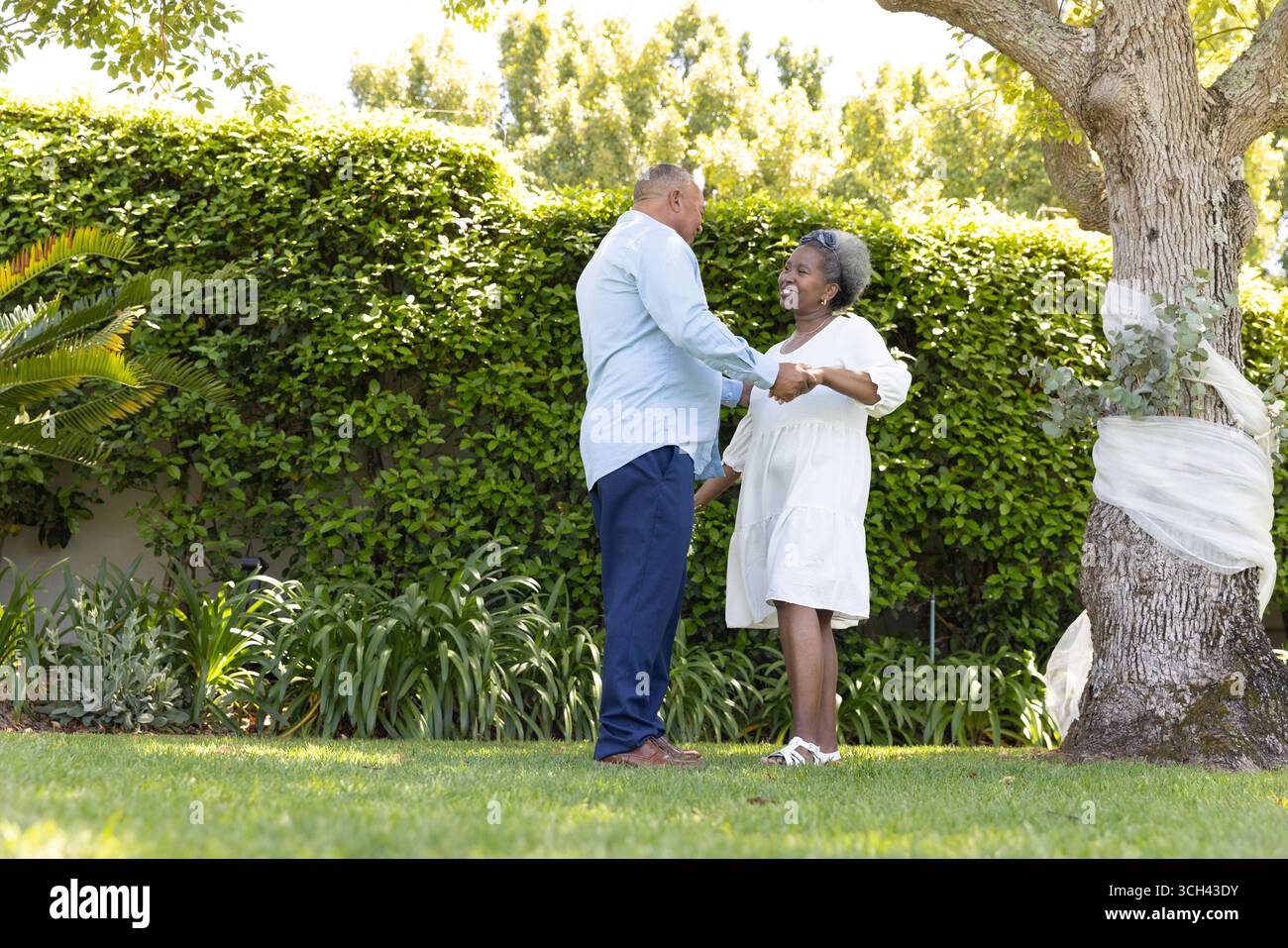 Couple senior dansant joyeusement ensemble dans le jardin ensoleillé, profitant du moment en plein air Banque D'Images