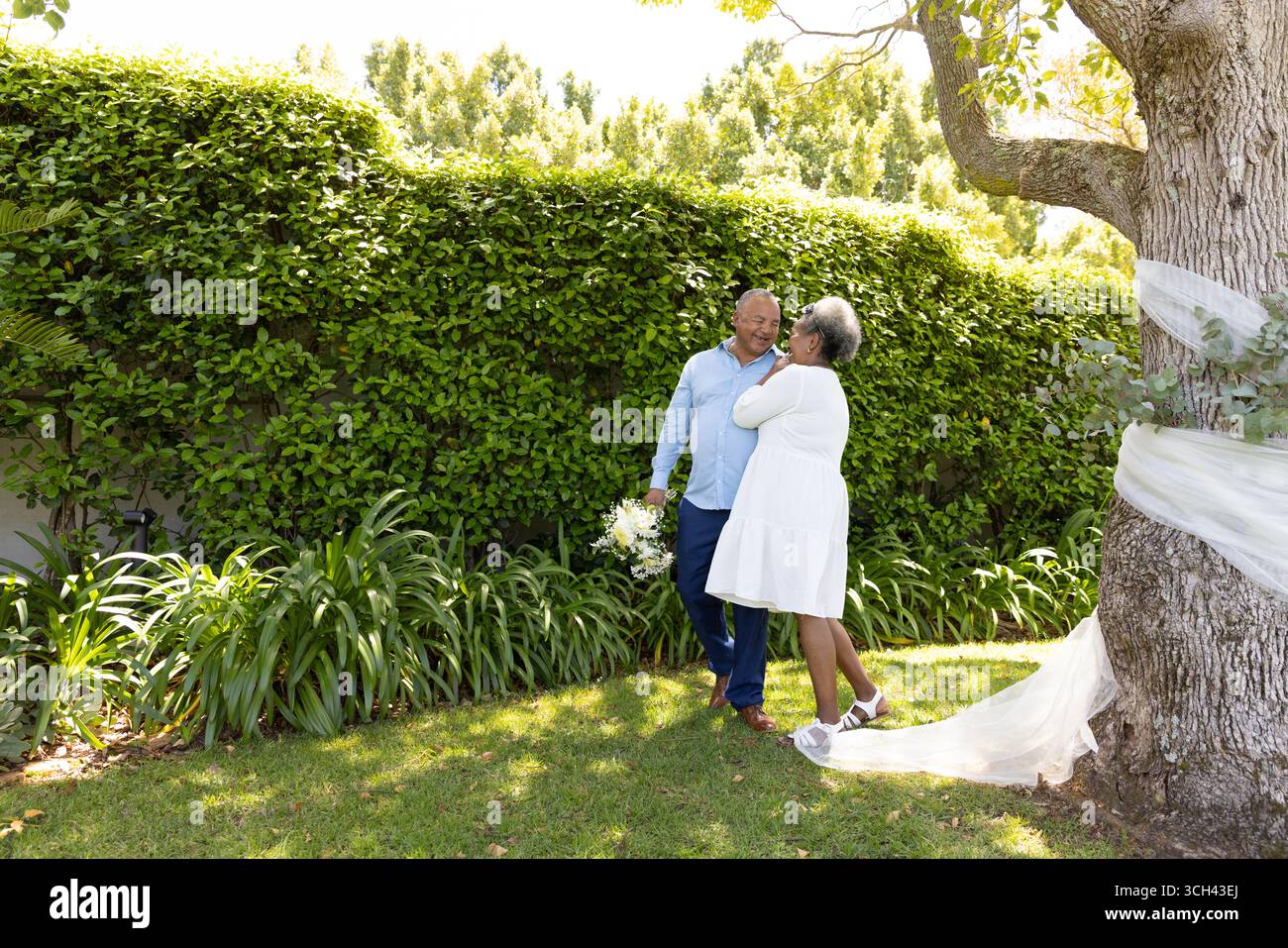 Couple senior embrassant sous l'arbre dans le jardin, profitant d'un moment romantique ensemble Banque D'Images