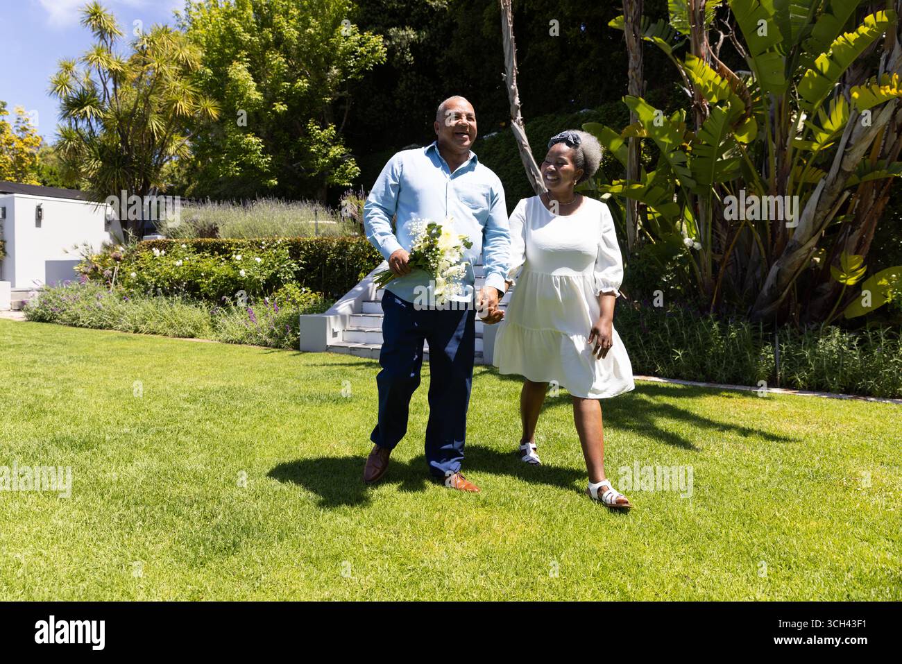 Couple senior marchant main dans la main dans le jardin ensoleillé, profitant de la promenade en plein air Banque D'Images