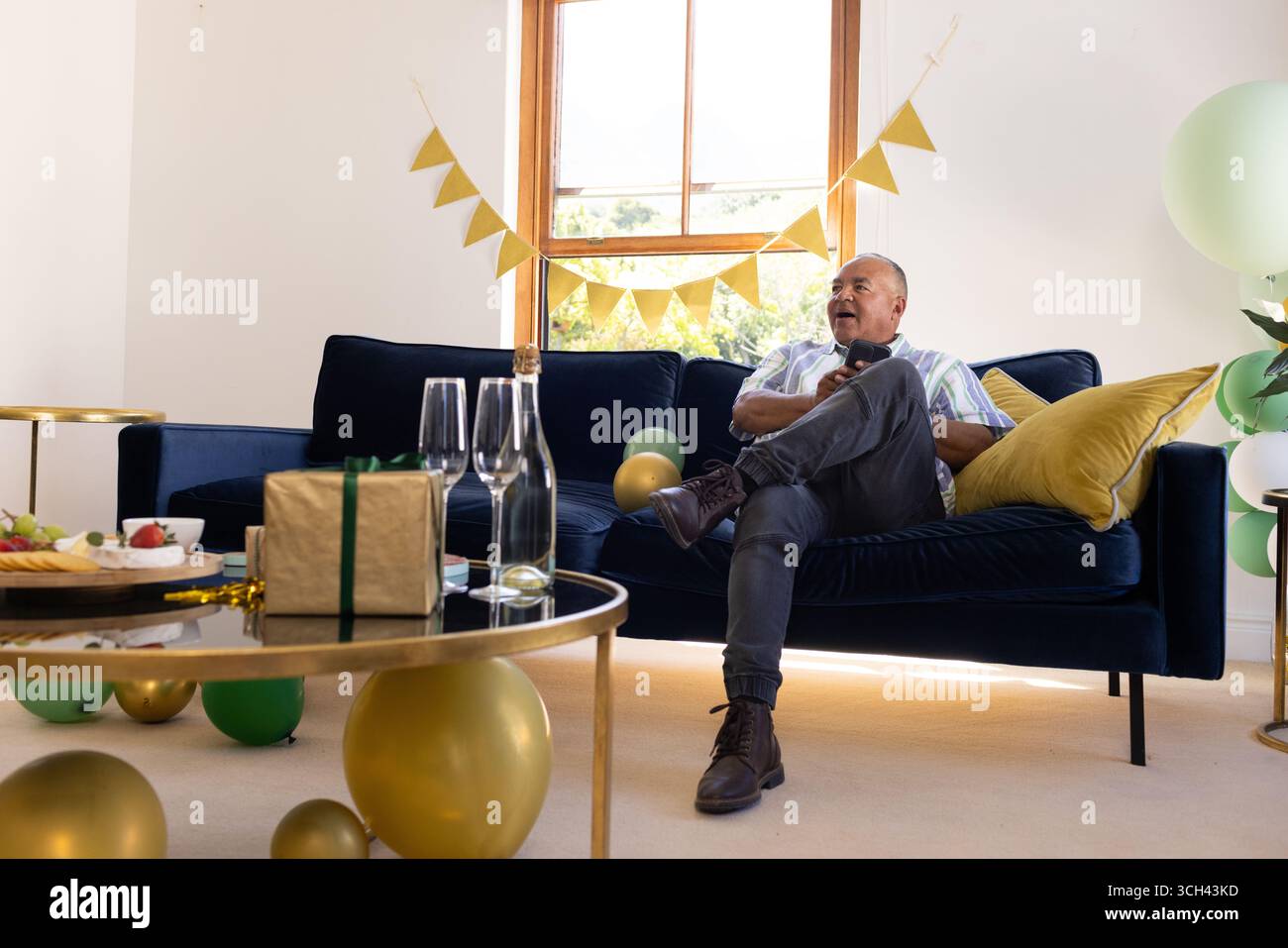 Homme senior se relaxant sur le canapé à la maison pendant la célébration festive avec des ballons Banque D'Images