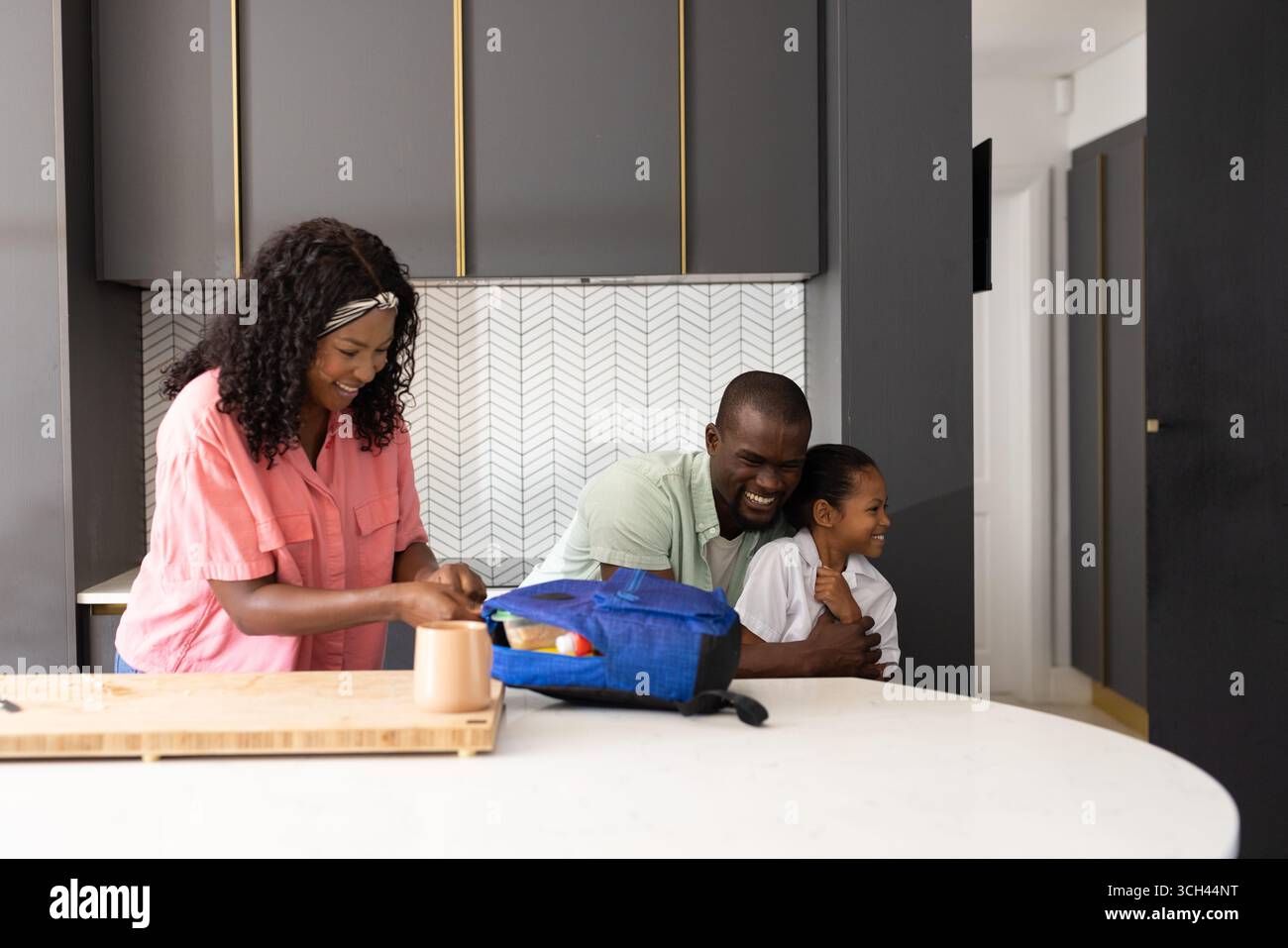 Dans la cuisine, les parents préparent le déjeuner tout en embrassant l'enfant, partageant un moment en famille Banque D'Images