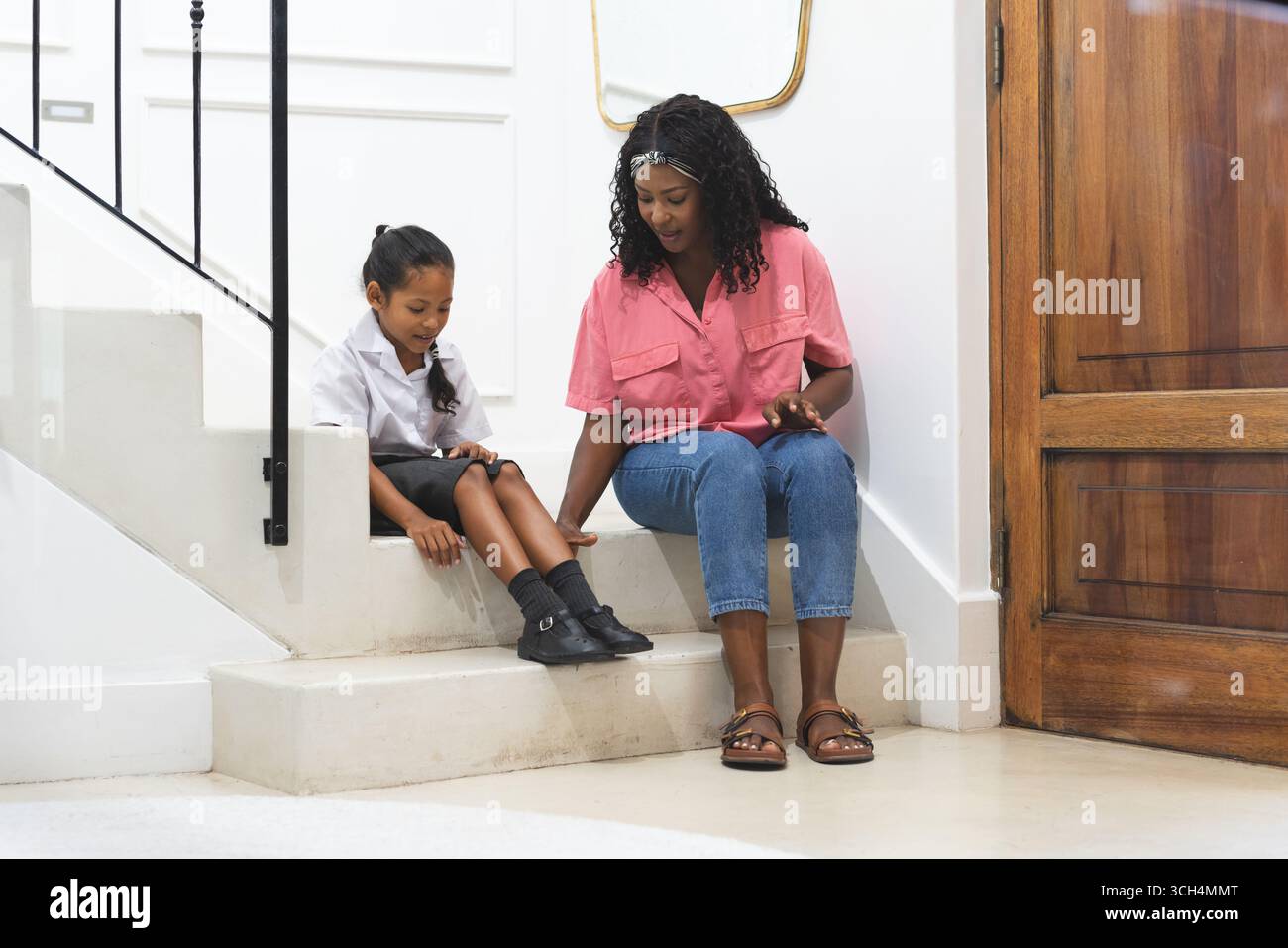 Avant l'école, mère et fille assises dans les escaliers, partageant un moment joyeux à la maison Banque D'Images Avant l'école, mère et fille assises dans les escaliers, partageant un moment joyeux à la maison Banque D'Images