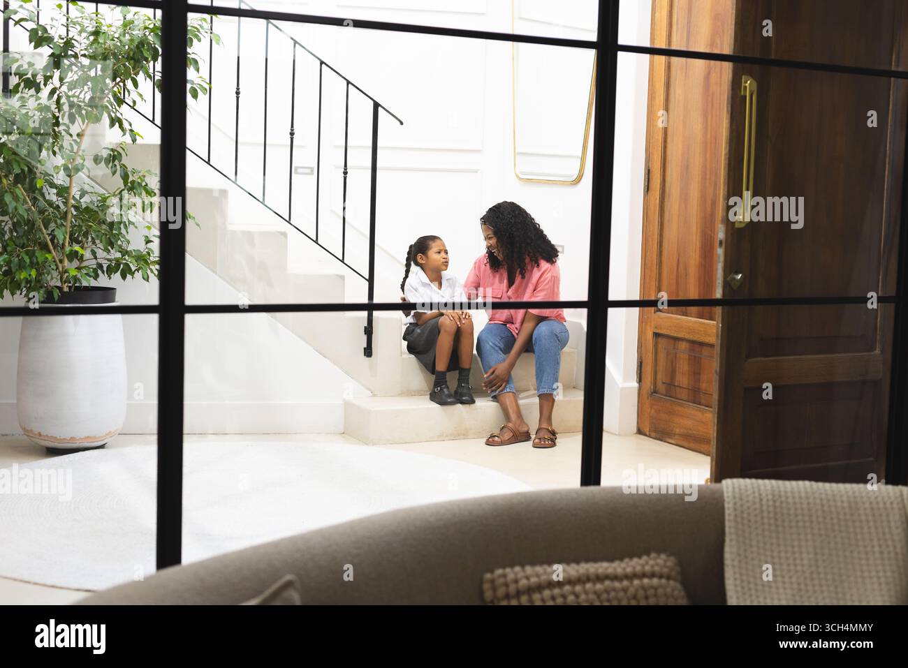 Avant l'école, mère et fille assis dans les escaliers à la maison, partageant une conversation sincère Banque D'Images Avant l'école, mère et fille assis dans les escaliers à la maison, partageant une conversation sincère Banque D'Images