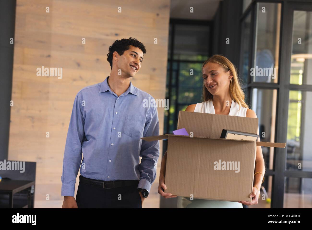 Collègues souriant tout en transportant la boîte dans le bureau moderne, appréciant le travail d'équipe Banque D'Images Collègues souriant tout en transportant la boîte dans le bureau moderne, appréciant le travail d'équipe Banque D'Images