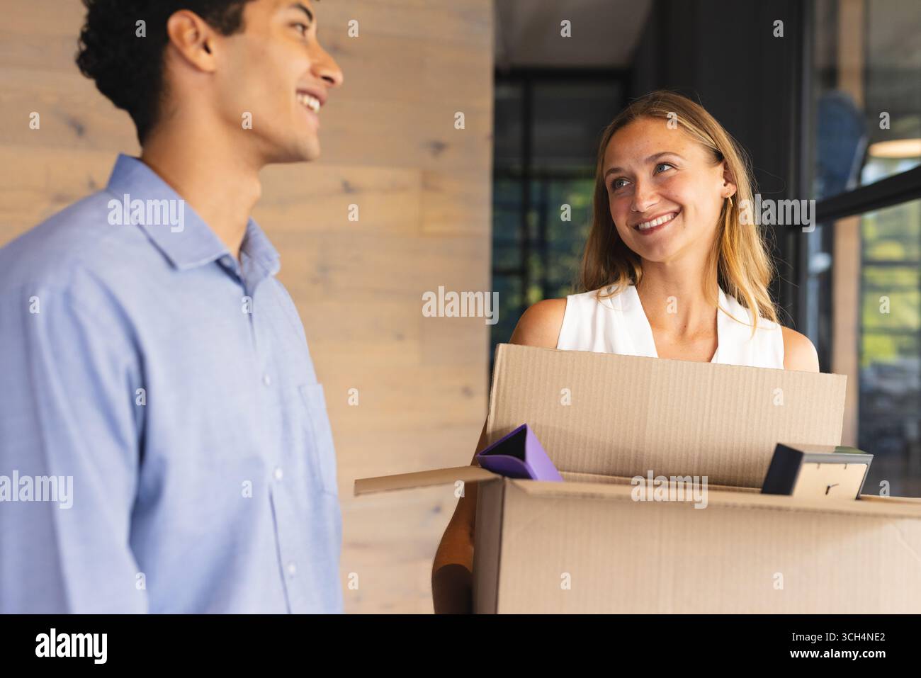 Collègues souriant tout en transportant des boîtes mobiles dans un cadre de bureau moderne Banque D'Images Collègues souriant tout en transportant des boîtes mobiles dans un cadre de bureau moderne Banque D'Images
