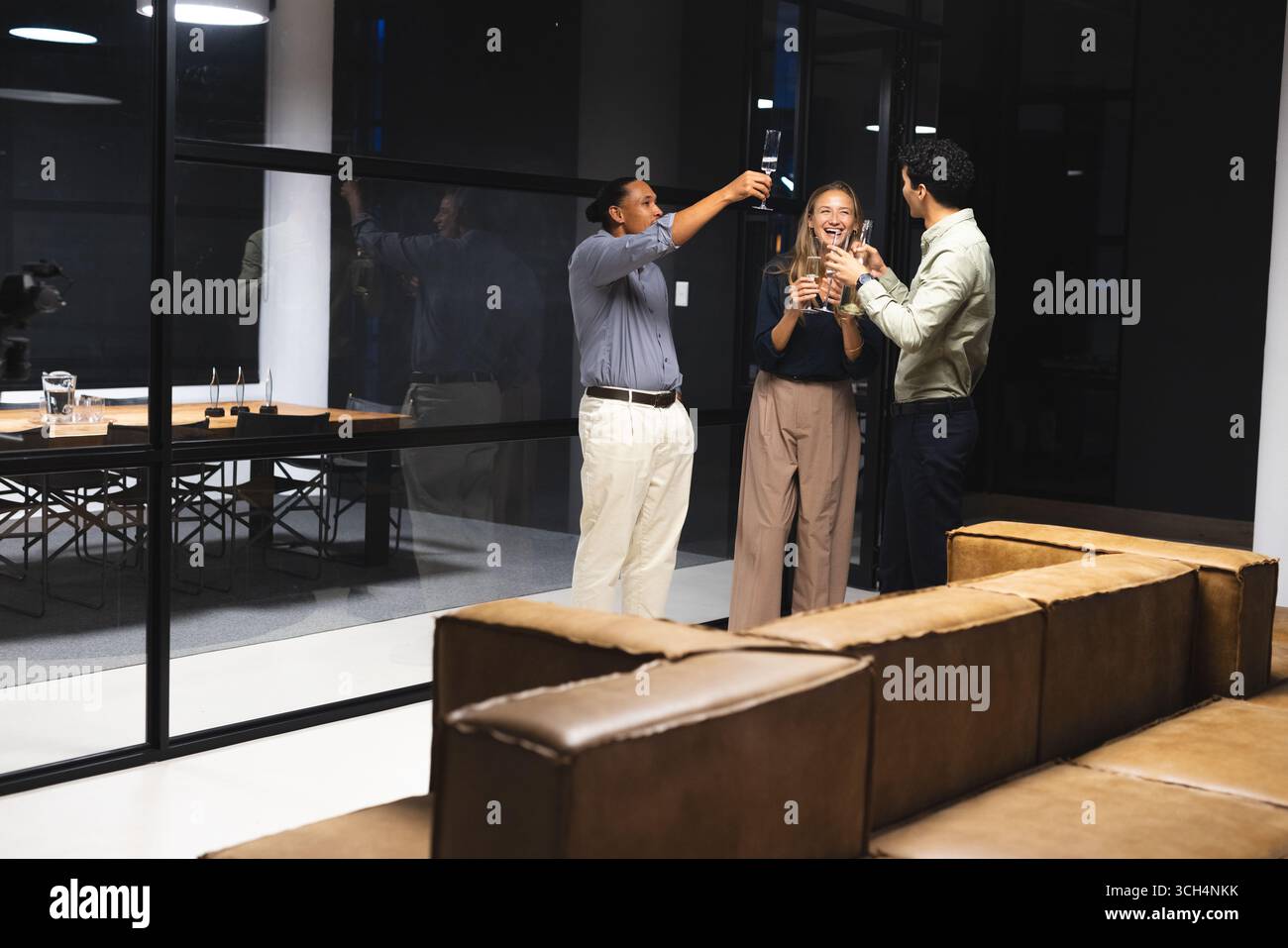 Collègues célébrant le succès avec un verre dans un bureau moderne la nuit Banque D'Images Collègues célébrant le succès avec un verre dans un bureau moderne la nuit Banque D'Images