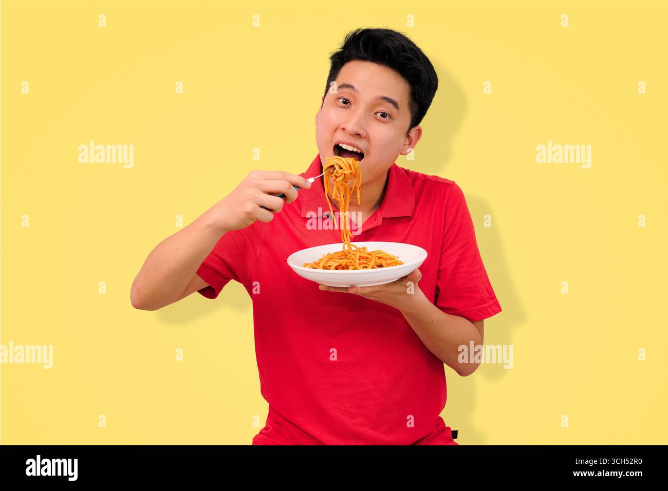 homme appréciant un repas de spaghetti avec une expression joyeuse sur fond jaune vif Banque D'Images