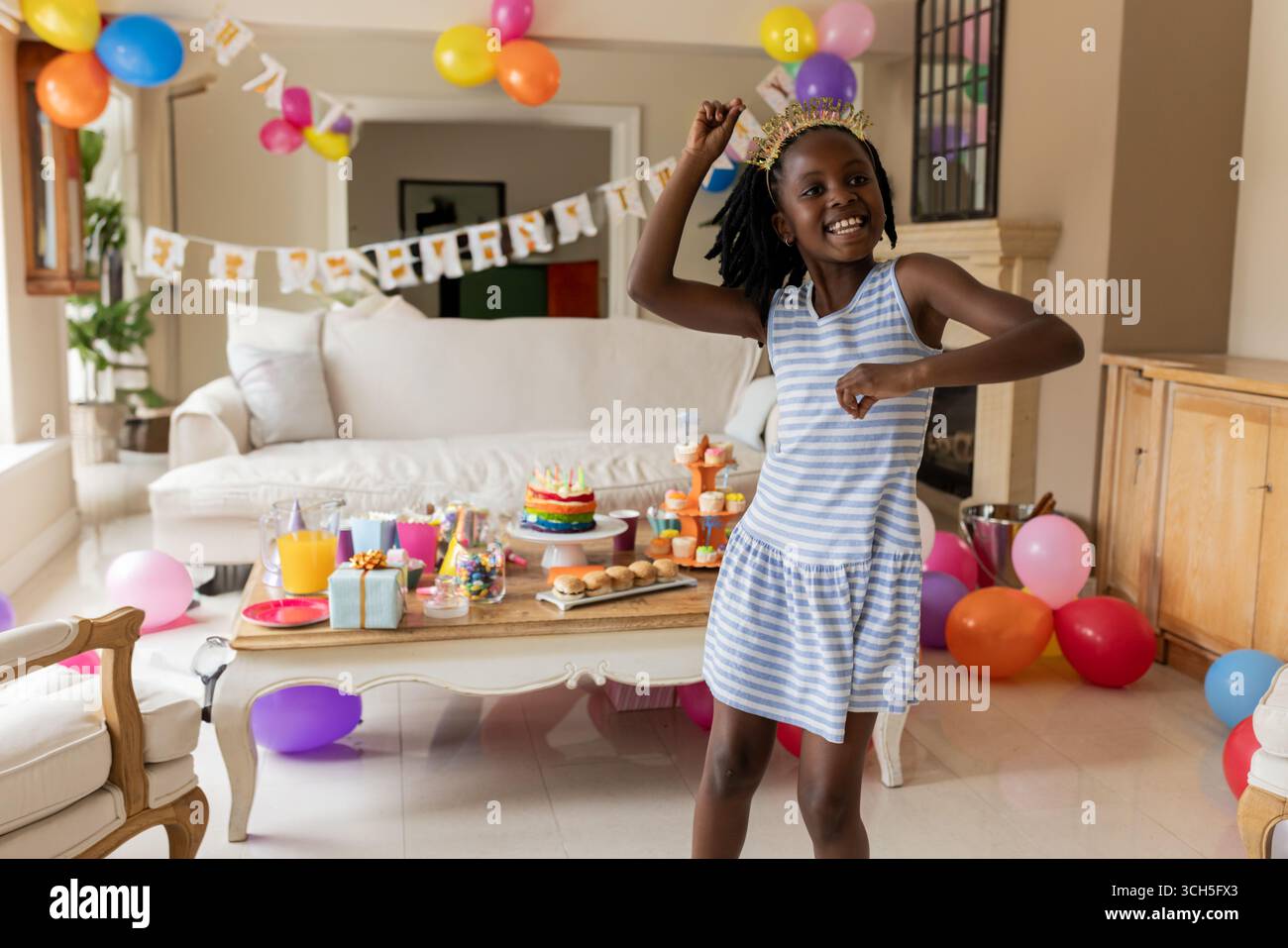 Fille afro-américaine dansant dans le salon, célébrant avec gâteau et ballons, espace de copie Banque D'Images