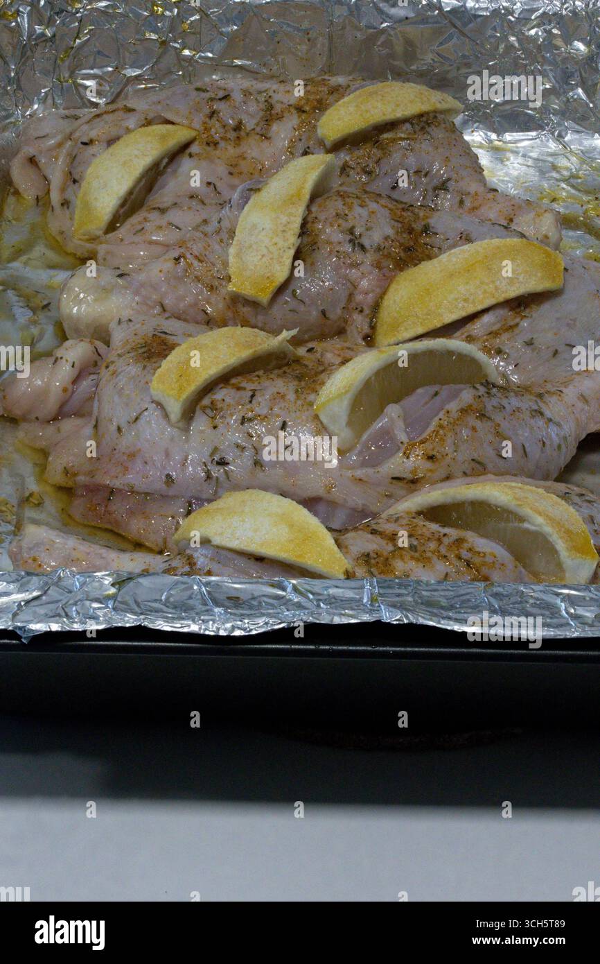 Morceaux de poulet cru avec quartiers de citron et herbes – préparation prête au four sur feuille d'aluminium Banque D'Images