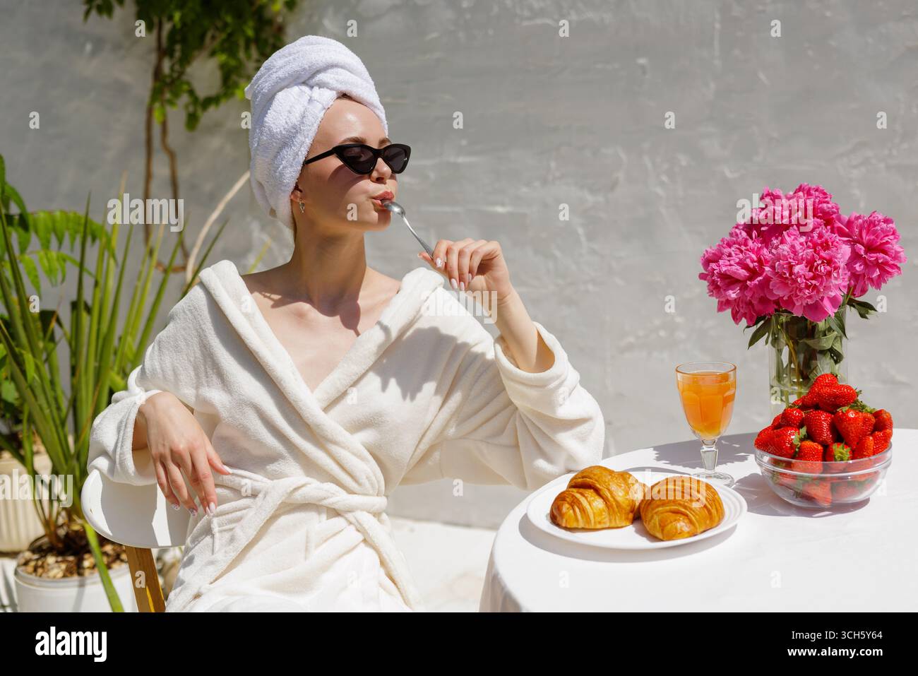 Femme appréciant le petit déjeuner de luxe avec des croissants et des fraises, se détendre en plein air dans une serviette et des lunettes de soleil, style de vie spa d'été Banque D'Images