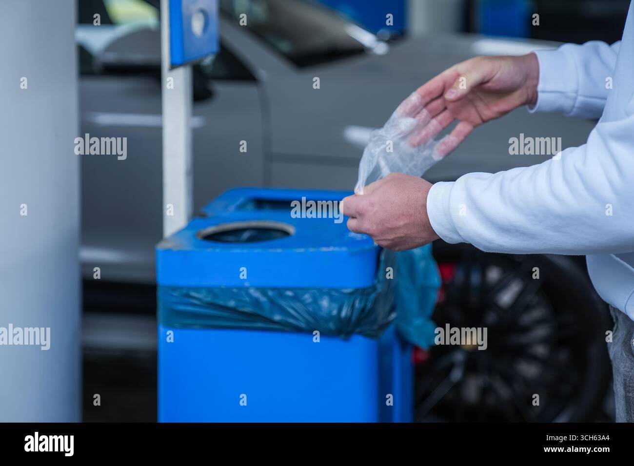 Homme jetant un gant jetable dans la poubelle d'une station-service Banque D'Images