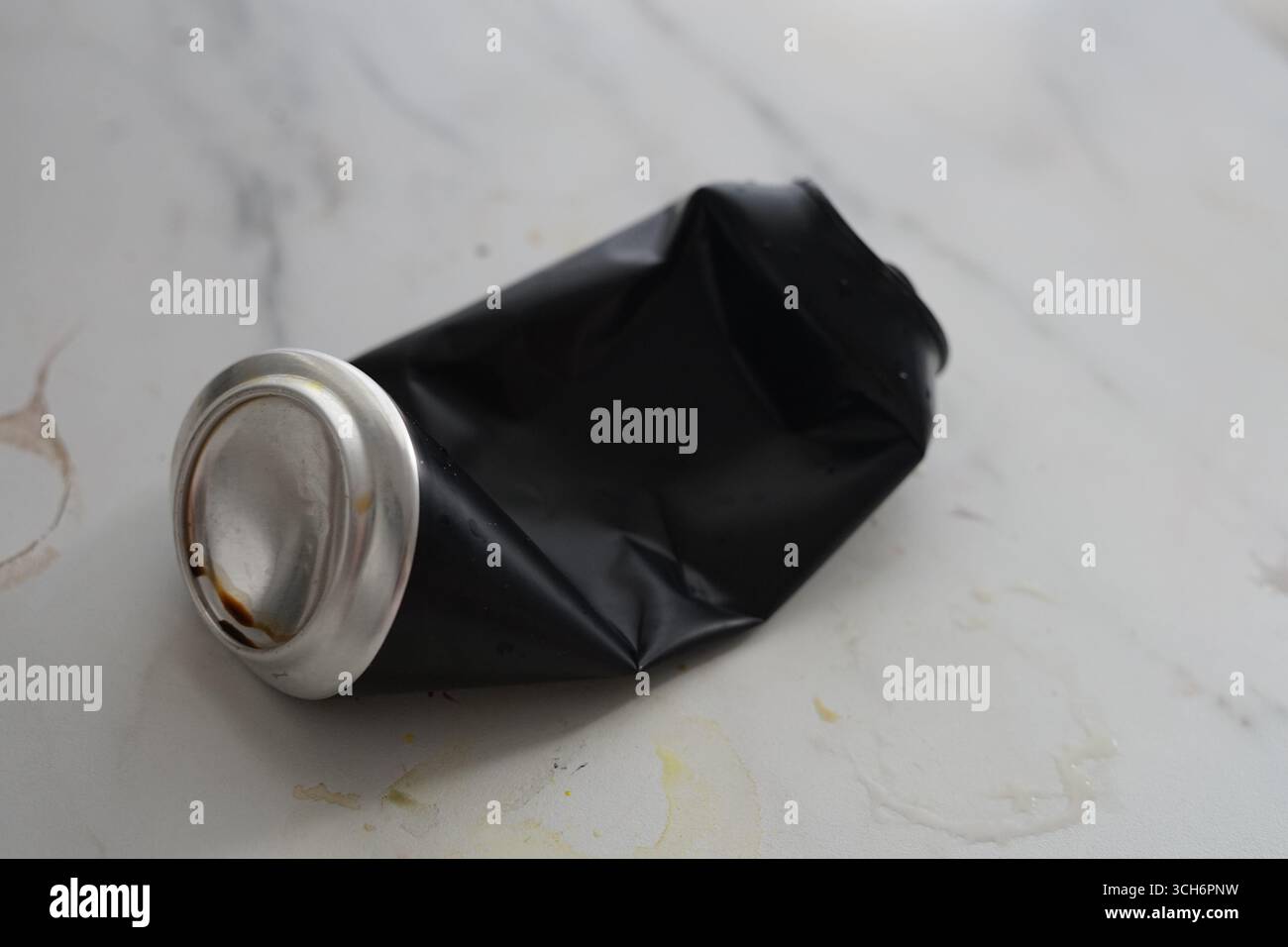 Un tube noir écrasé avec un rebord argenté est placé sur une surface en marbre, créant un contraste visuel intéressant. Banque D'Images