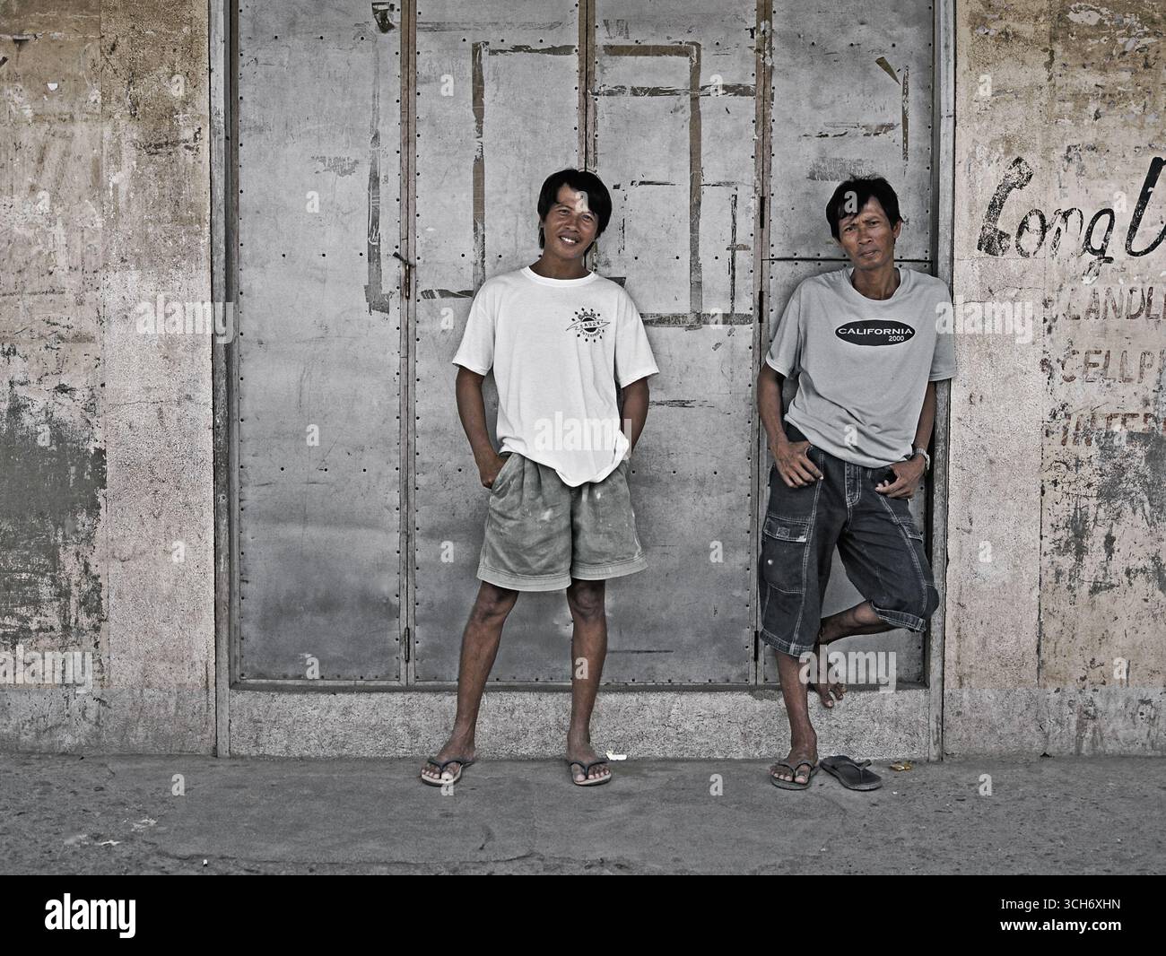 Deux adultes philippins séjournant à l'ombre le long d'une route rurale, attendant un bus par une journée tranquille dans un village des Philippines. Un moment franc réfléchit Banque D'Images