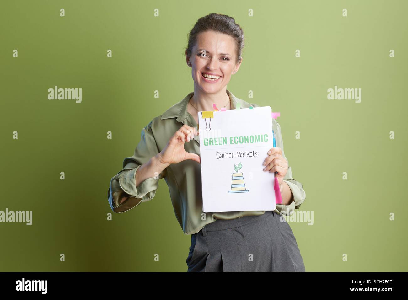 Femme souriante avec des papiers Green Economic Carbon Markets faisant une forme de cœur, véhiculant la positivité vers la durabilité environnementale. Banque D'Images