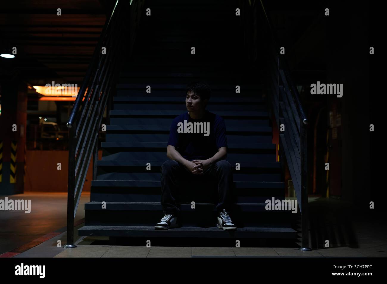 Un jeune homme monte un escalier sombre dans un environnement urbain sombre, portant un sac à dos Banque D'Images