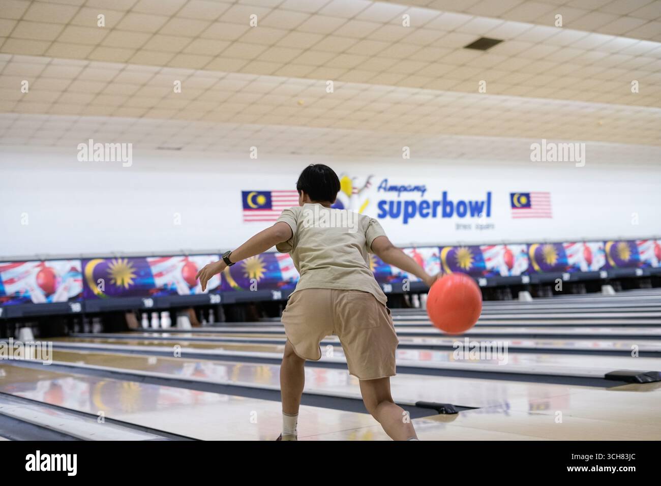 Un joueur de bowling concentré lance une balle en haut arc sur une piste de bowling polie dans une ruelle intérieure vibrante Banque D'Images