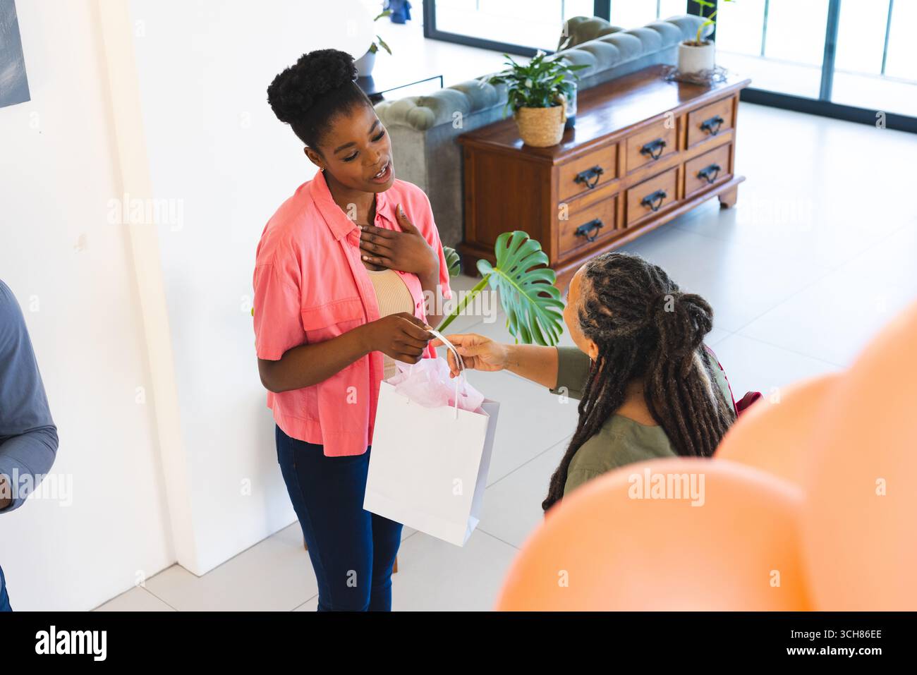 Femme recevant un sac cadeau à la maison, souriant et se sentant surprise pendant la célébration Banque D'Images