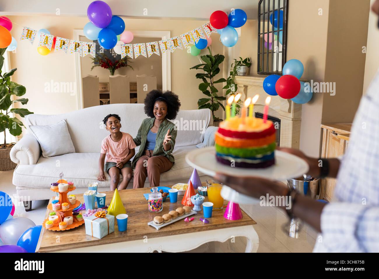 À la fête, mère afro-américaine et enfant célébrant l'anniversaire à la maison avec un gâteau coloré Banque D'Images À la fête, mère afro-américaine et enfant célébrant l'anniversaire à la maison avec un gâteau coloré Banque D'Images