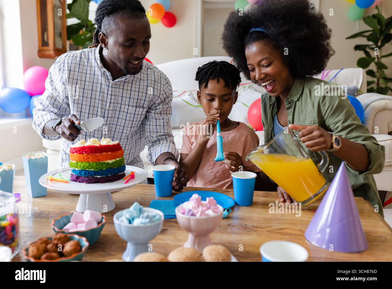À la fête, célébrer l'anniversaire à la maison, enfant soufflant la corne de fête, parents servant des boissons Banque D'Images À la fête, célébrer l'anniversaire à la maison, enfant soufflant la corne de fête, parents servant des boissons Banque D'Images